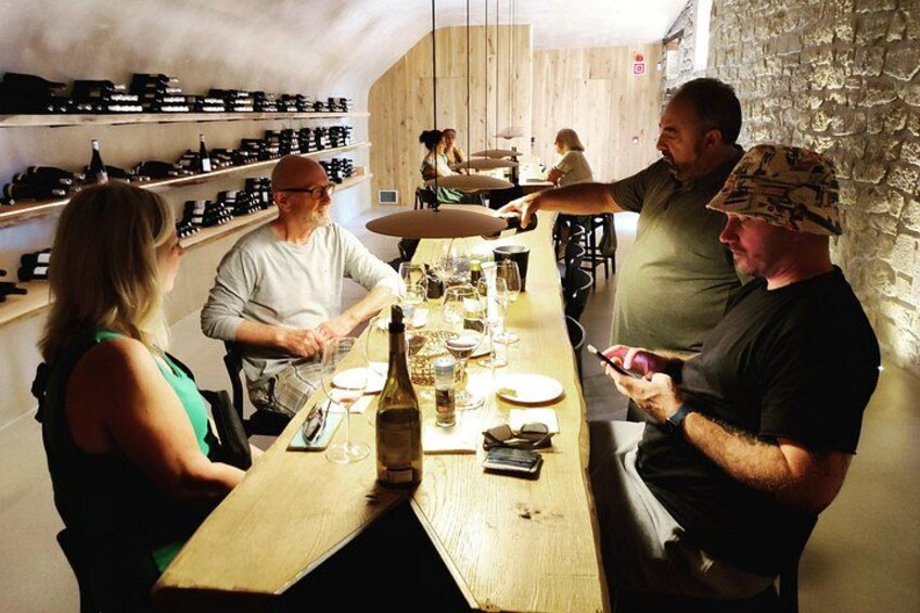 A wooden bar with bottles and glasses, a person holding a phone, and another person pouring a drink. 1