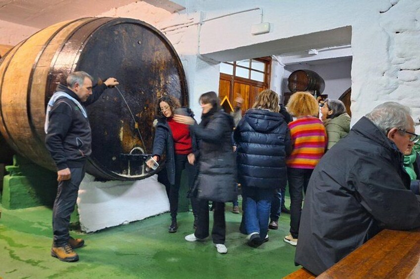 A group of people inspecting a large, rusted metal barrel in a room with white walls and a green floor. 4