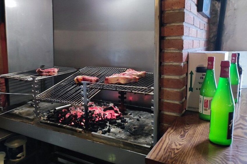 A grill with meat and charcoal. There are green bottles on the right. 3