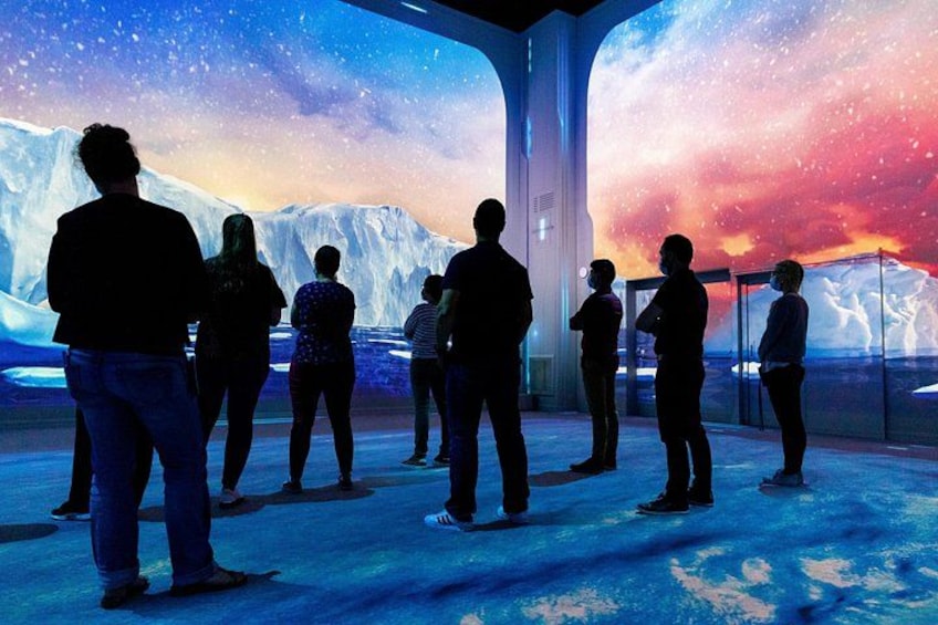People standing in a room with a large digital display of a snowy landscape and a starry sky. 5