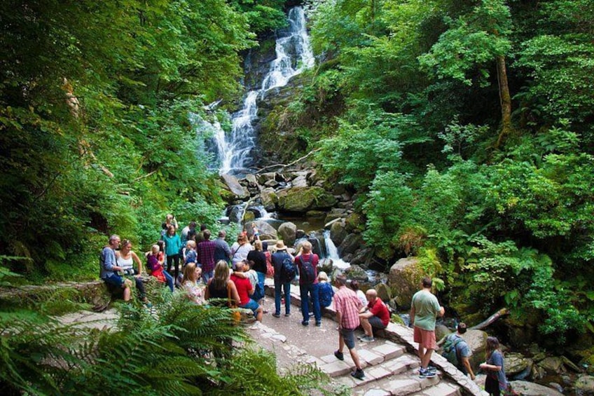 A group of people hiking near a waterfall in a forested area. 2