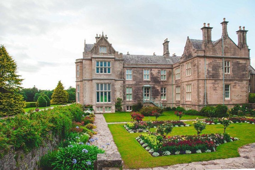 A large stone building with multiple chimneys, surrounded by well-maintained gardens and a stone pathway. 3