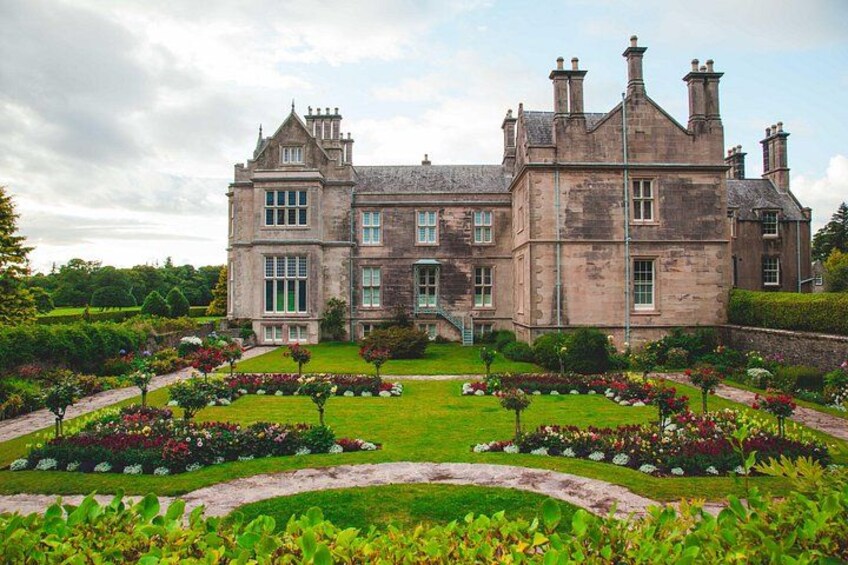 A large stone building with a symmetrical facade, surrounded by well-manicured gardens and a clear sky. 2