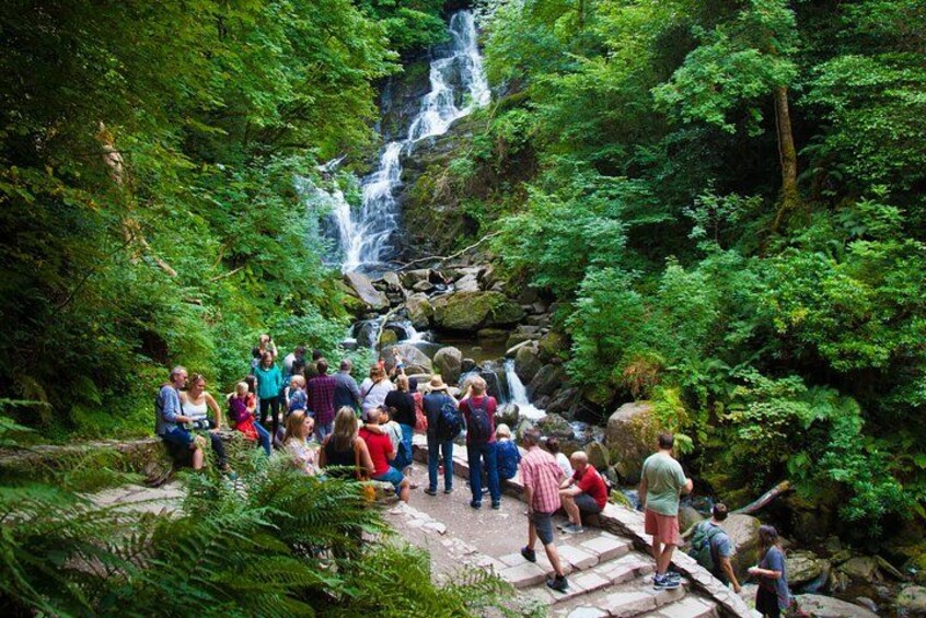 A group of people hiking near a waterfall in a forested area. 2