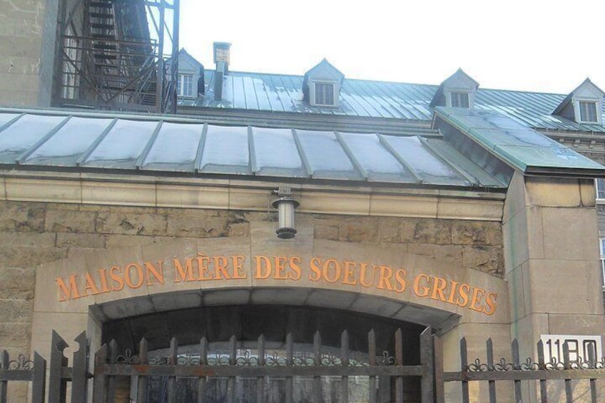 A building with the sign 'MAISON MERE DES SOEURS GRIS' and a metal fence in front. 4