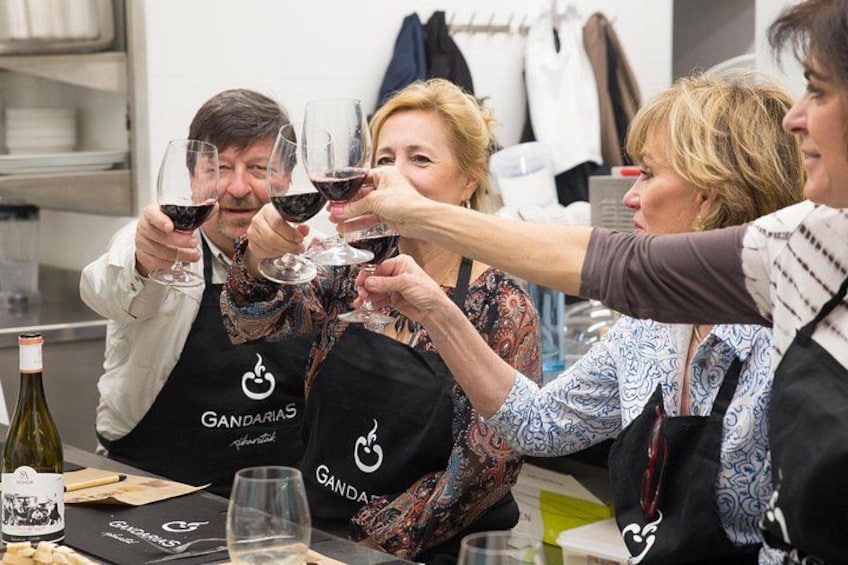 Un gruppo di persone brinda con bicchieri di vino, indossando grembiuli con il logo 'Gandarias'. 2