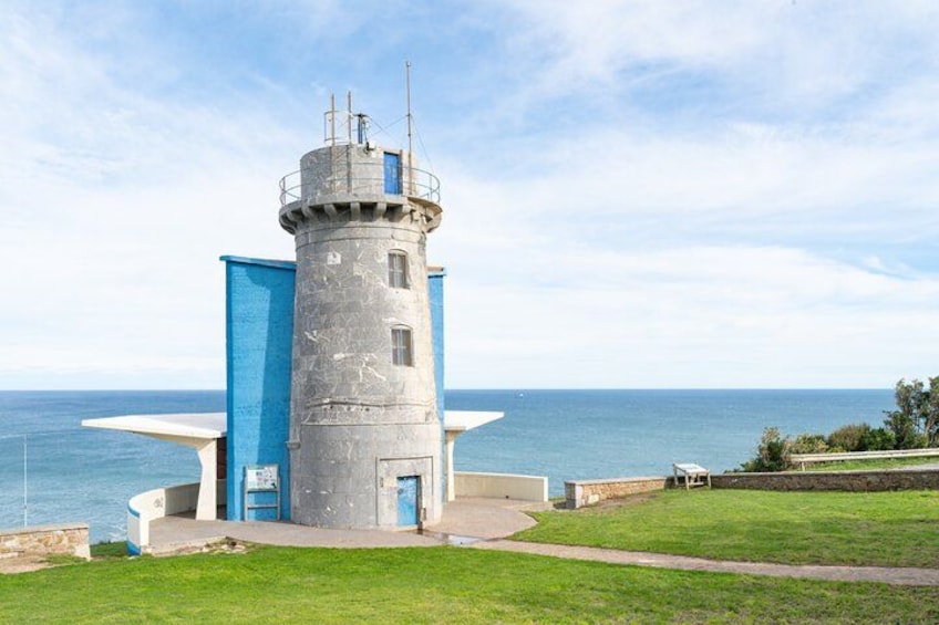 Een vuurtoren met een cilindrische toren en een blauwe constructie ernaast, met uitzicht op de zee. 5