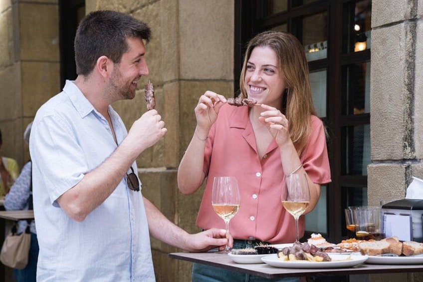 Zwei Personen essen draußen und halten Essen und Weingläser in der Hand. 1