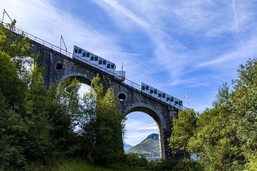A stone bridge with a train crossing over it, surrounded by greenery and a clear sky. 2