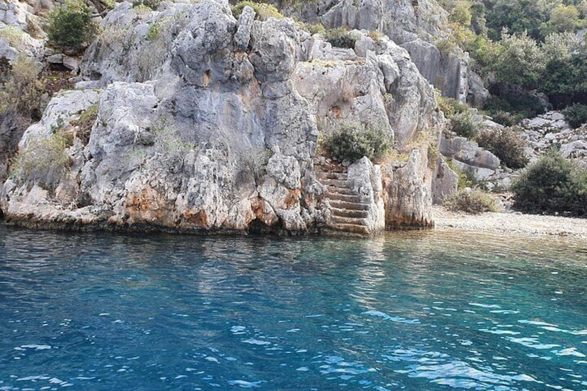 A rocky coastline with clear blue water, a stone staircase, and sparse vegetation. 3