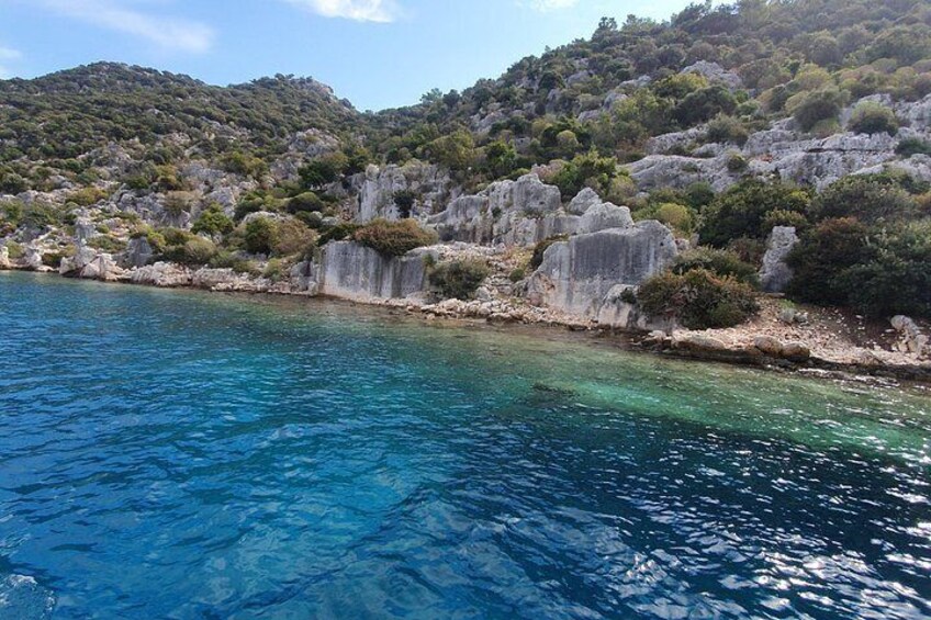 A coastal landscape with clear blue water, rocky cliffs, and green vegetation. 4