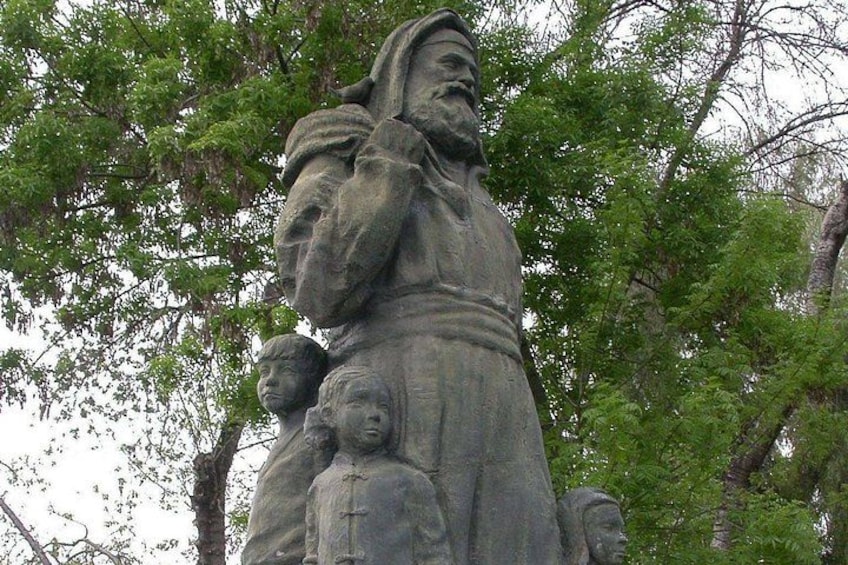 A stone statue of a man with a child, set against a backdrop of trees. 5