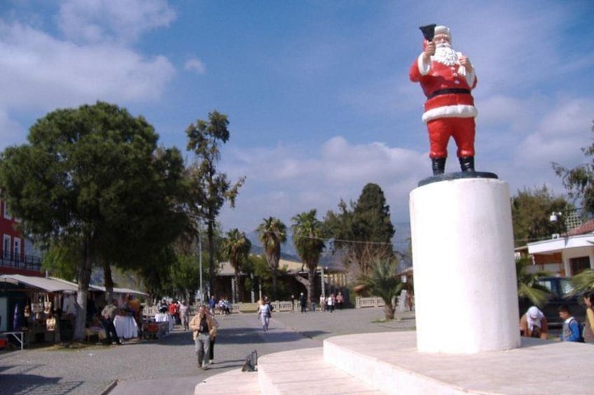 A statue of Santa Claus on a pedestal in a public square with trees and buildings in the background. 4