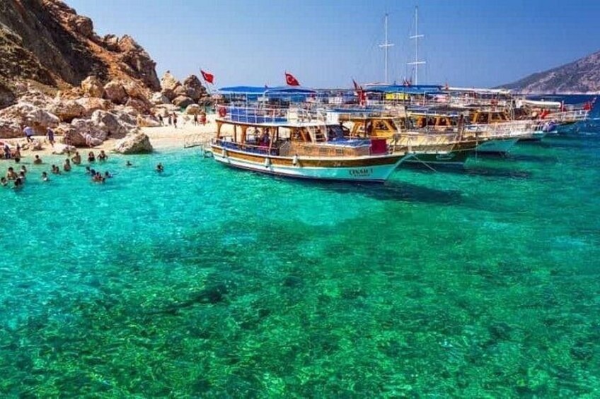 Helder turquoise water met boten, rotsachtige kliffen en een strand. 2