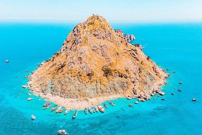 Een rotsachtig eiland omringd door turquoise water, met verschillende boten afgemeerd nabij de kust. 4