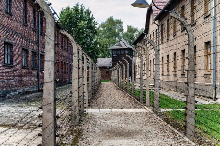 A long, narrow pathway flanked by brick buildings with barbed wire fencing. 5
