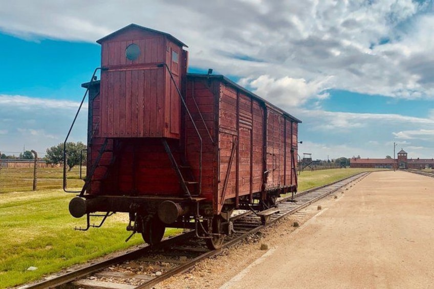 Un vagón de ferrocarril color rojo, tipo cabina de maquinista, sobre rieles, con un cielo despejado y un campo verde al fondo. 2