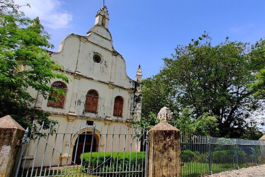 A historic church with a bell tower, surrounded by a metal fence and greenery. 1