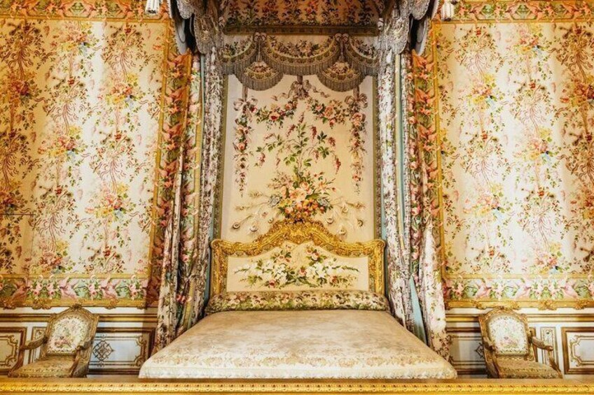 An ornate bed with floral wallpaper, a canopy, and gold accents. 2