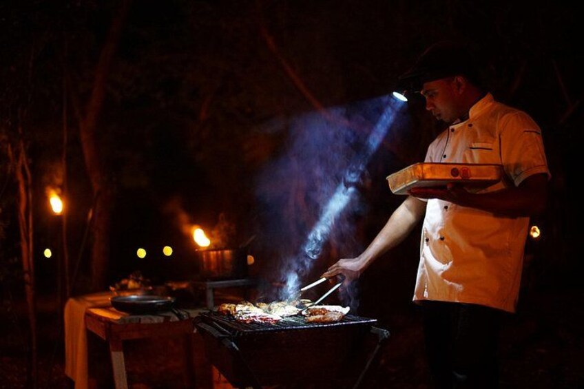 A chef grilling outdoors at night with a portable grill and a table with a pan. 5