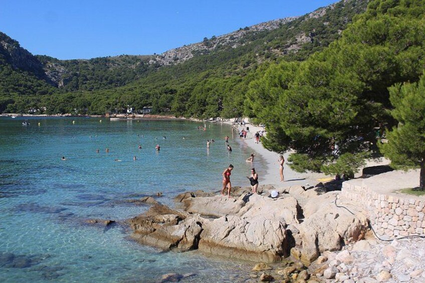 Una playa costera con agua cristalina, costa rocosa y gente nadando y tomando el sol. 3