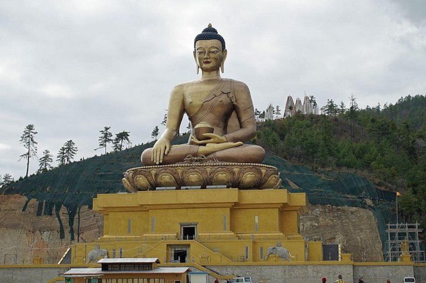 En stor sittande Buddha-staty på en piedestal, omgiven av en tempelbyggnad och ett bergigt landskap. 3