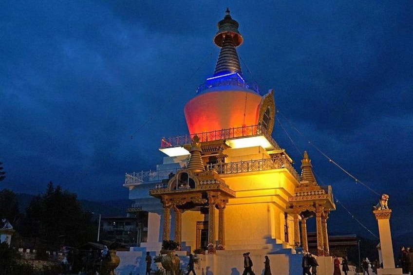 A brightly lit stupa with a multi-tiered structure, surrounded by a temple complex with statues and architectural details. 2