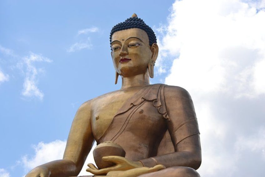 En stor sittande Buddha-staty med händerna i en meditationsställning, placerad mot en klarblå himmel. 1