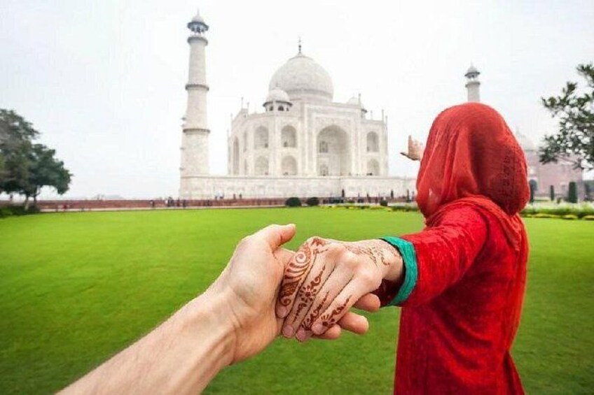 En person klädd i rött håller handen med en annan person, med Taj Mahal i bakgrunden. 1