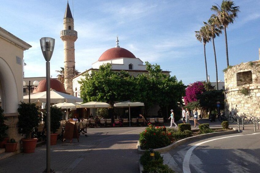 Une rue bordée de terrasses, une mosquée avec un minaret, des palmiers et un ciel dégagé. 4