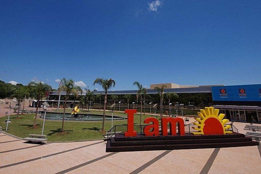 Un cartel grande con la frase 'I am', un gráfico de sol, una piscina, palmeras y un edificio al fondo. 2