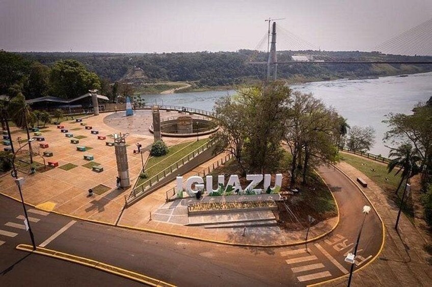 Un parque con un monumento circular, un puente al fondo y un río. 5
