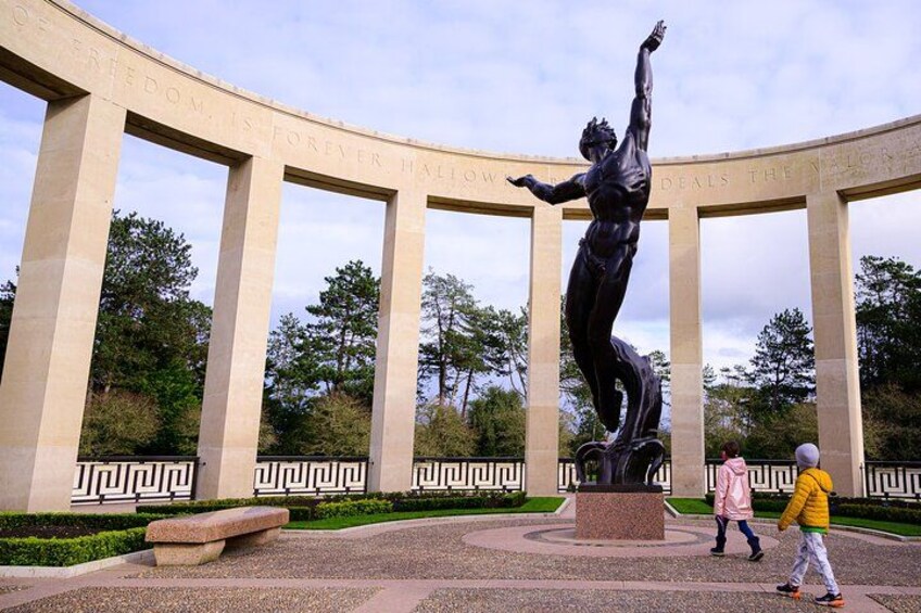 Une statue se dresse sur une place circulaire, ornée de colonnes, et est entourée de verdure ainsi que d’une allée pavée. 3