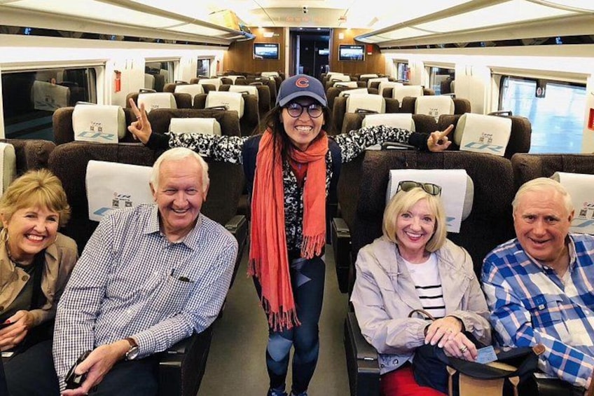 Un grupo de personas sentadas en un vagón de tren con almacenaje superior y espacio personal. 2