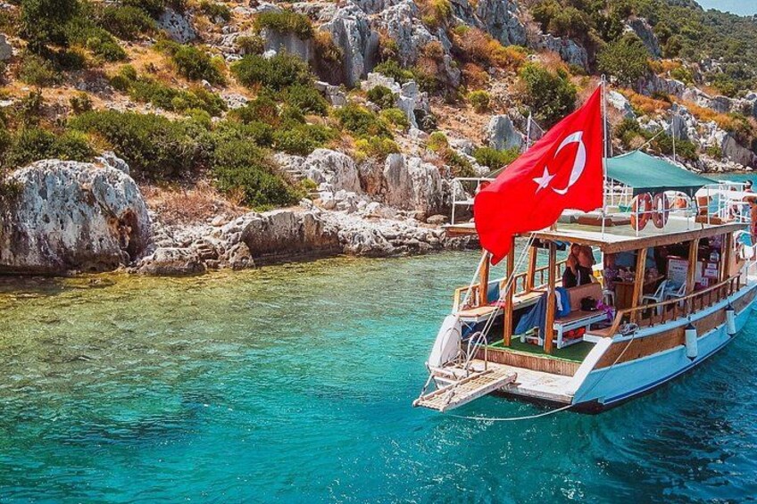Een boot met een Turkse vlag, een rotsachtige kustlijn en helder turquoise water. 5