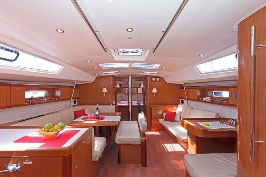 A well-lit interior of a yacht with wooden cabinetry, a dining area, and a seating area with cushions. 3