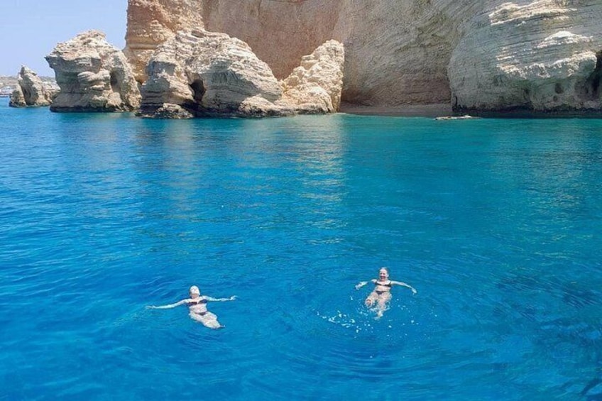 Two people swimming in clear blue water with rocky cliffs in the background. 4