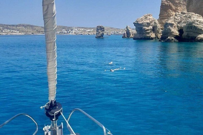 A sailboat with a clear blue sea, rocky cliffs, and a distant island. 5