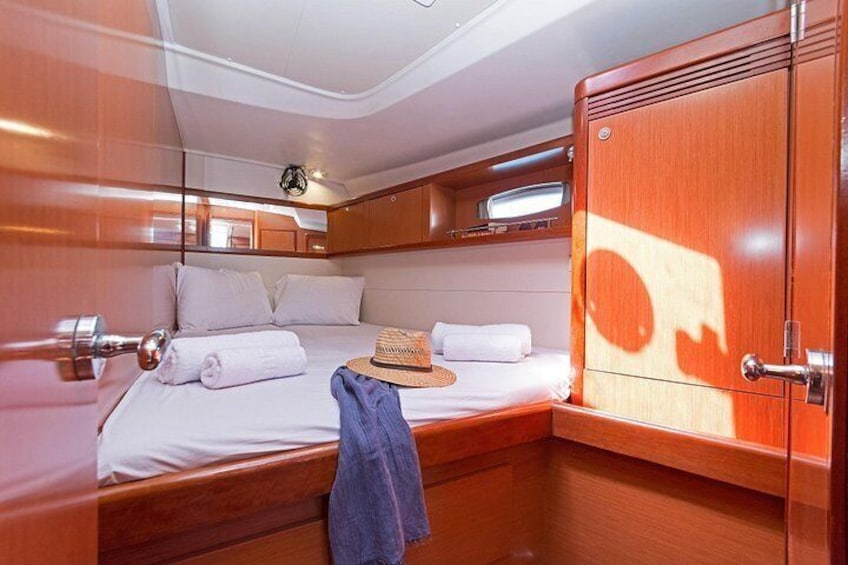 A cabin with wooden walls, a bed with white linens, a hat on the bed, and a towel on the floor. 2