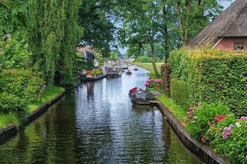 A narrow canal with boats, lush greenery, and a thatched-roof building. 5