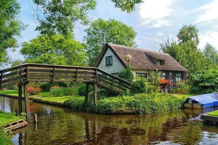 A house with a thatched roof, a wooden bridge over a canal, and lush greenery. 4