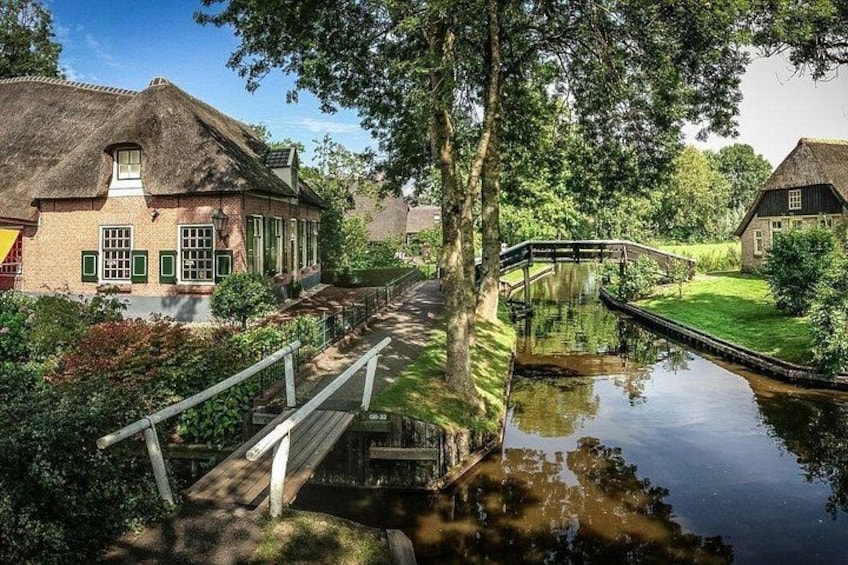A canal with a wooden bridge, a thatched-roof house, and lush greenery. 3