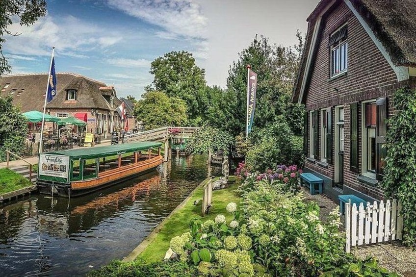 A canal with a boat, a bridge, a building, and a garden. 1