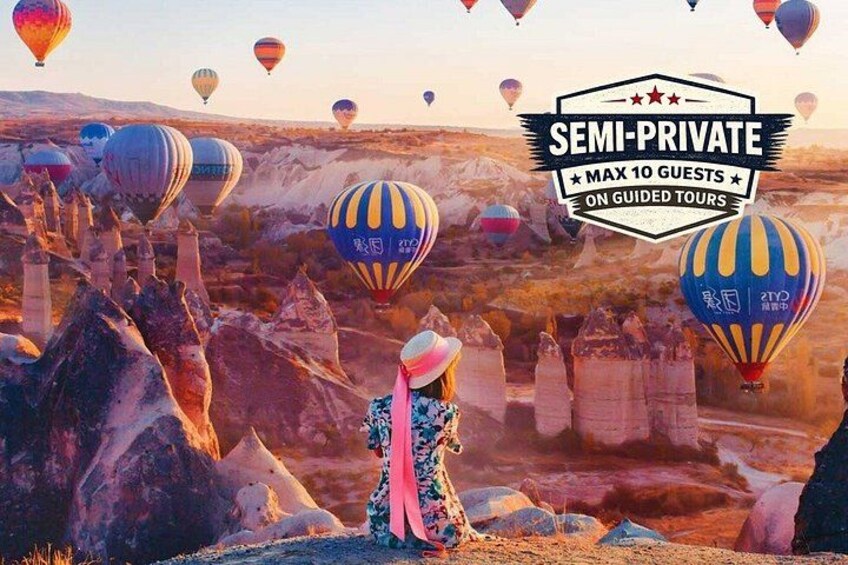 A desert landscape with hot air balloons, a person in traditional attire, and a sign indicating a semi-private tour with a maximum of 10 guests. 1