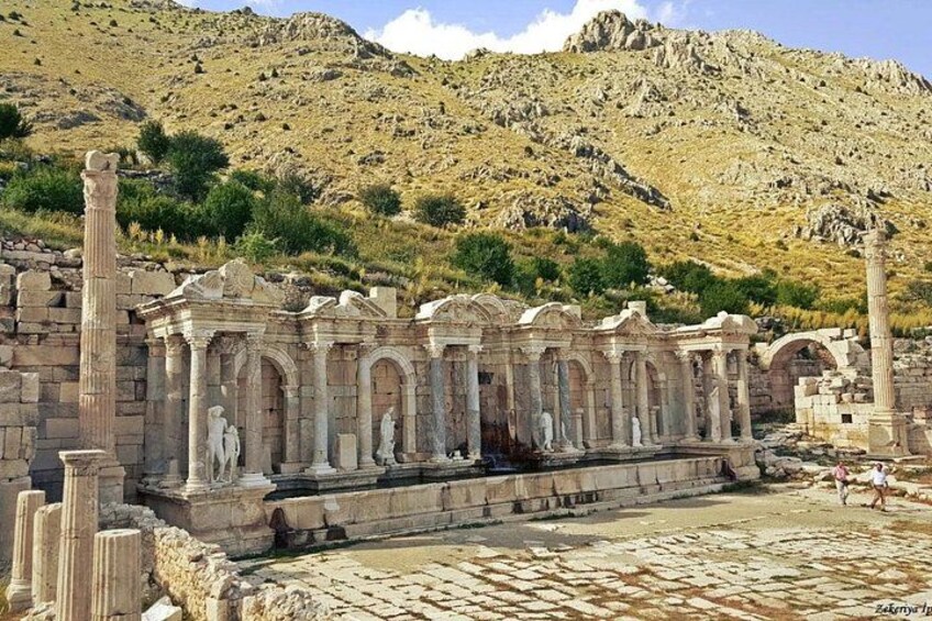 Ruinas antiguas con columnas y estatuas, al pie de montañas imponentes. 5