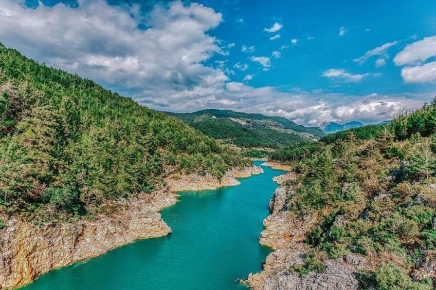 Un río turquesa serpenteando por un valle boscoso flanqueado por riscos rocosos. 3