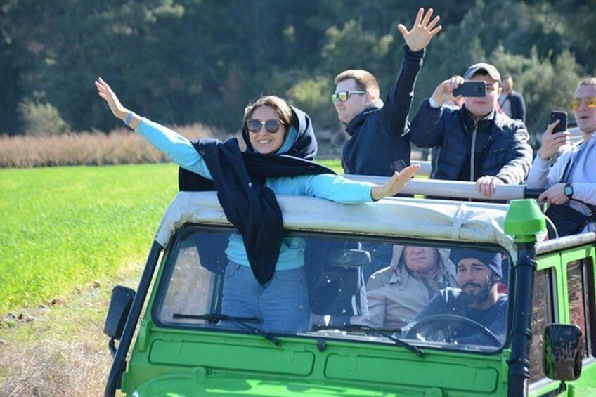 A green vehicle with people on top, some waving. 1