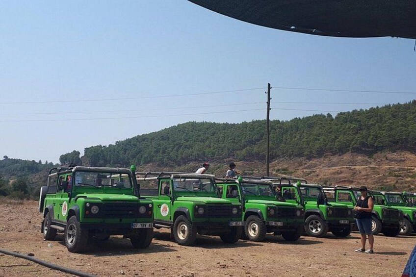 A row of green vehicles parked on a dirt road with a hilly landscape in the background. 5