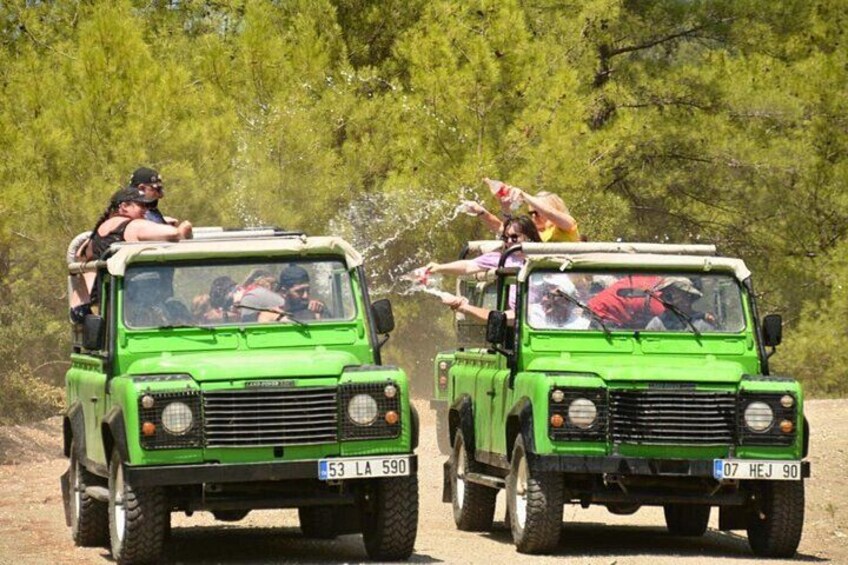 Two green off-road vehicles with people on top, driving on a dirt road. 3