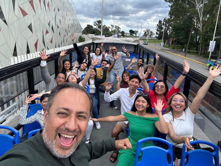 A group of people on a boat with raised hands, a geometric patterned wall, and a cloudy sky. 3